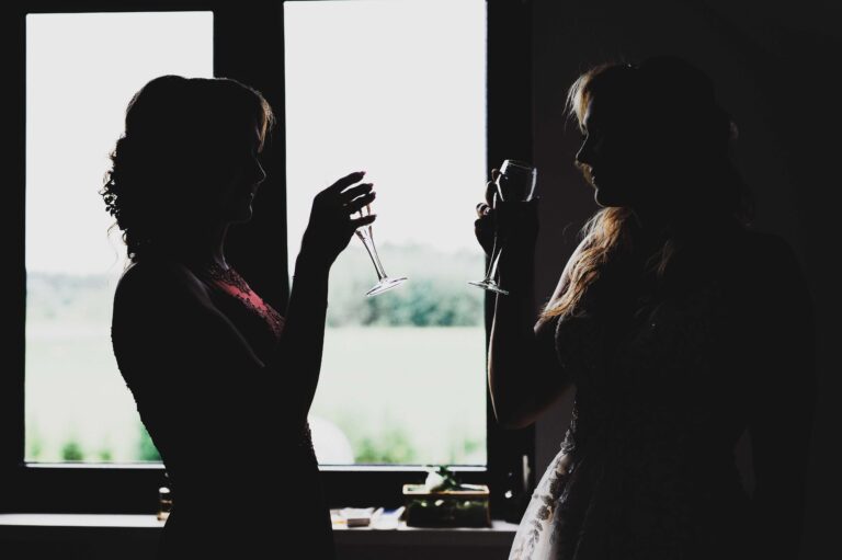 Świadkowa i panna młoda piją szampana na tle okna