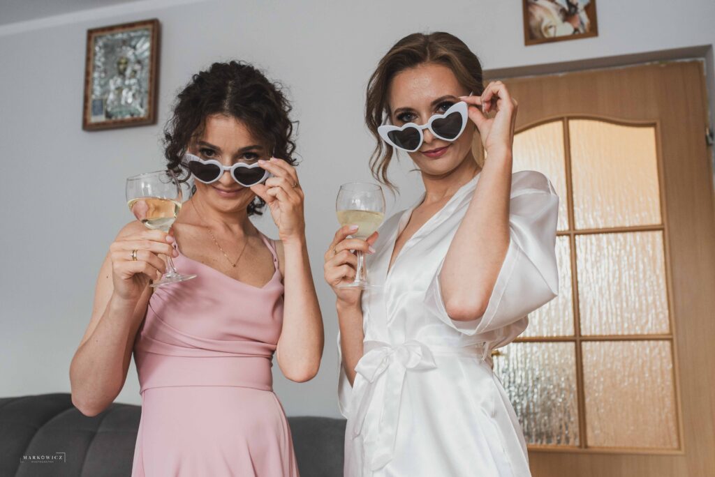 Panna młoda i świadkowa w trakcie przygotowań pija szampana i się wygłupiają